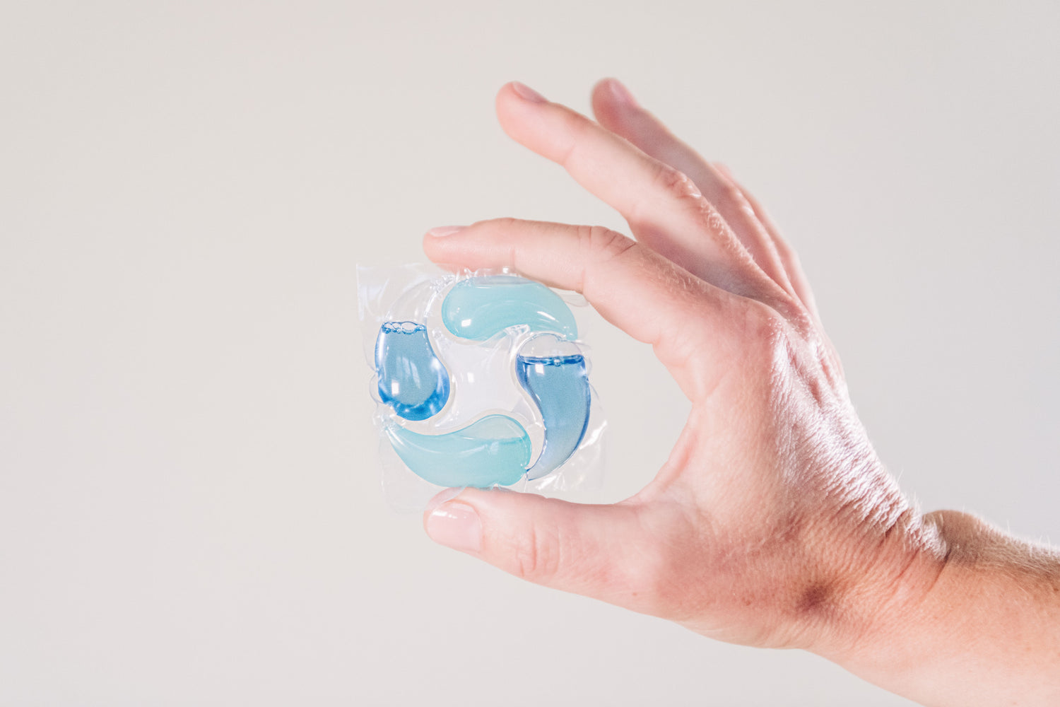 Hand holding a clear gelatinous object with blue swirling patterns against a light gray background