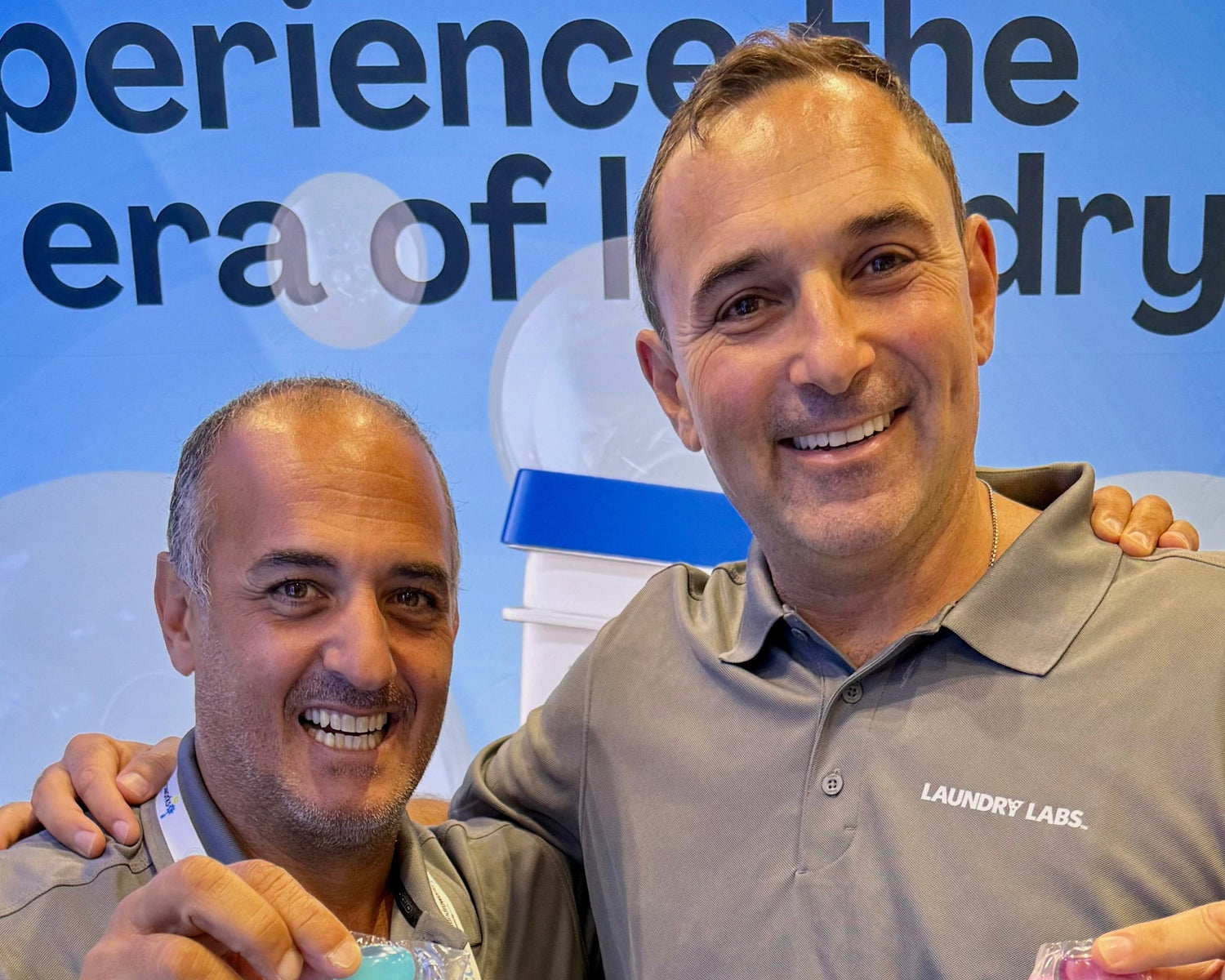 Two men posing together with a backdrop featuring text and logos.
