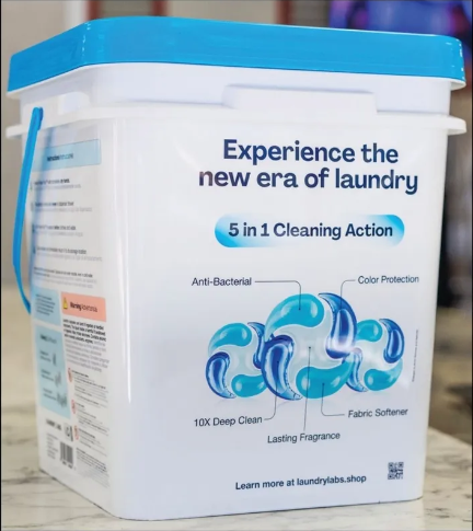 White laundry detergent bucket with blue lid and label on a wooden surface